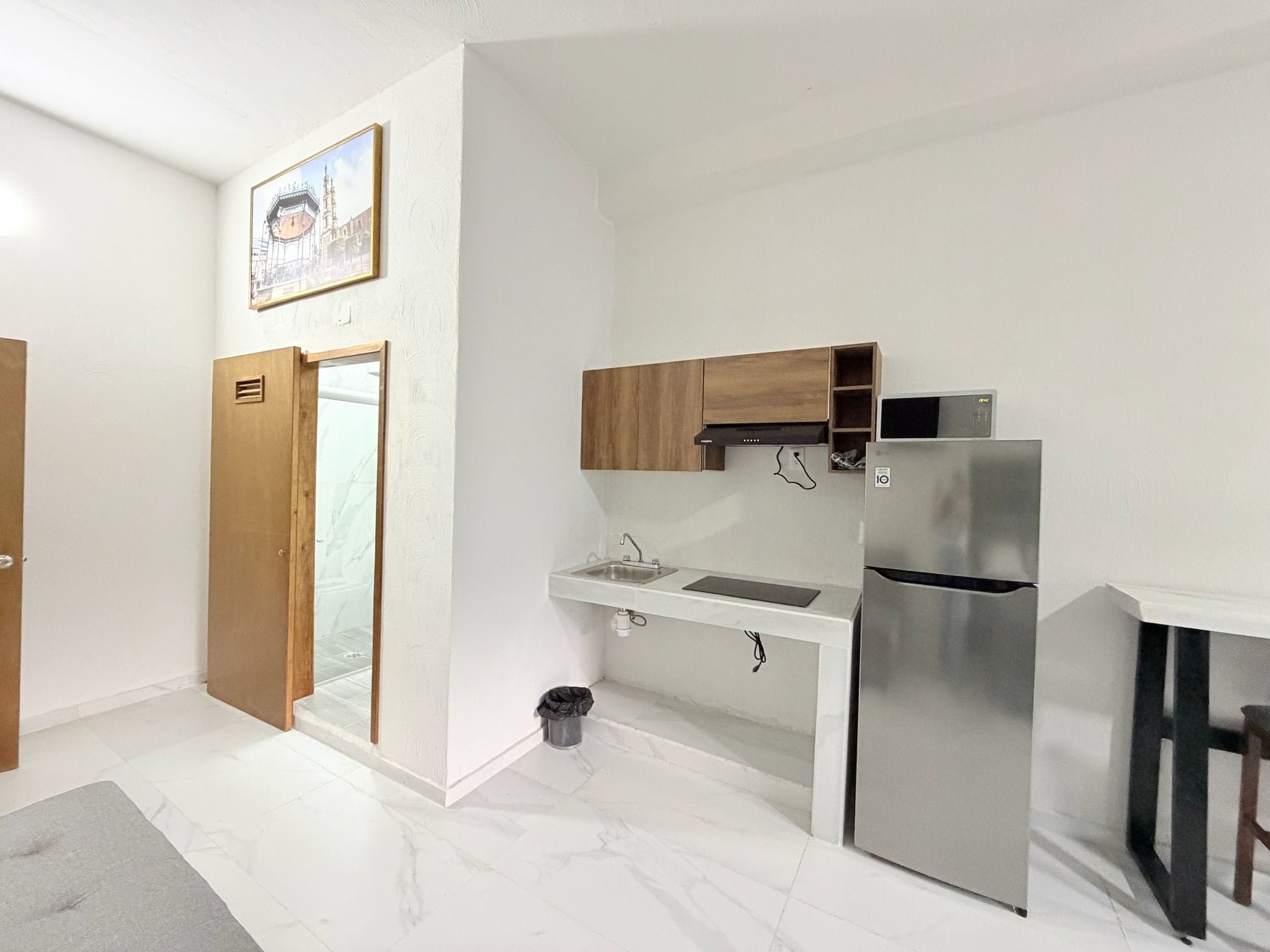 Cocina compacta con refrigerador integrado, lavamanos y muebles de madera.