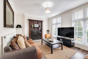 Ein Wohnzimmer mit Sofa, Couchtisch, Kamin, Fernseher und großen Fenstern.