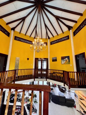 A spacious interior with a high ceiling, a central chandelier, and a balcony overlooking a lower level.