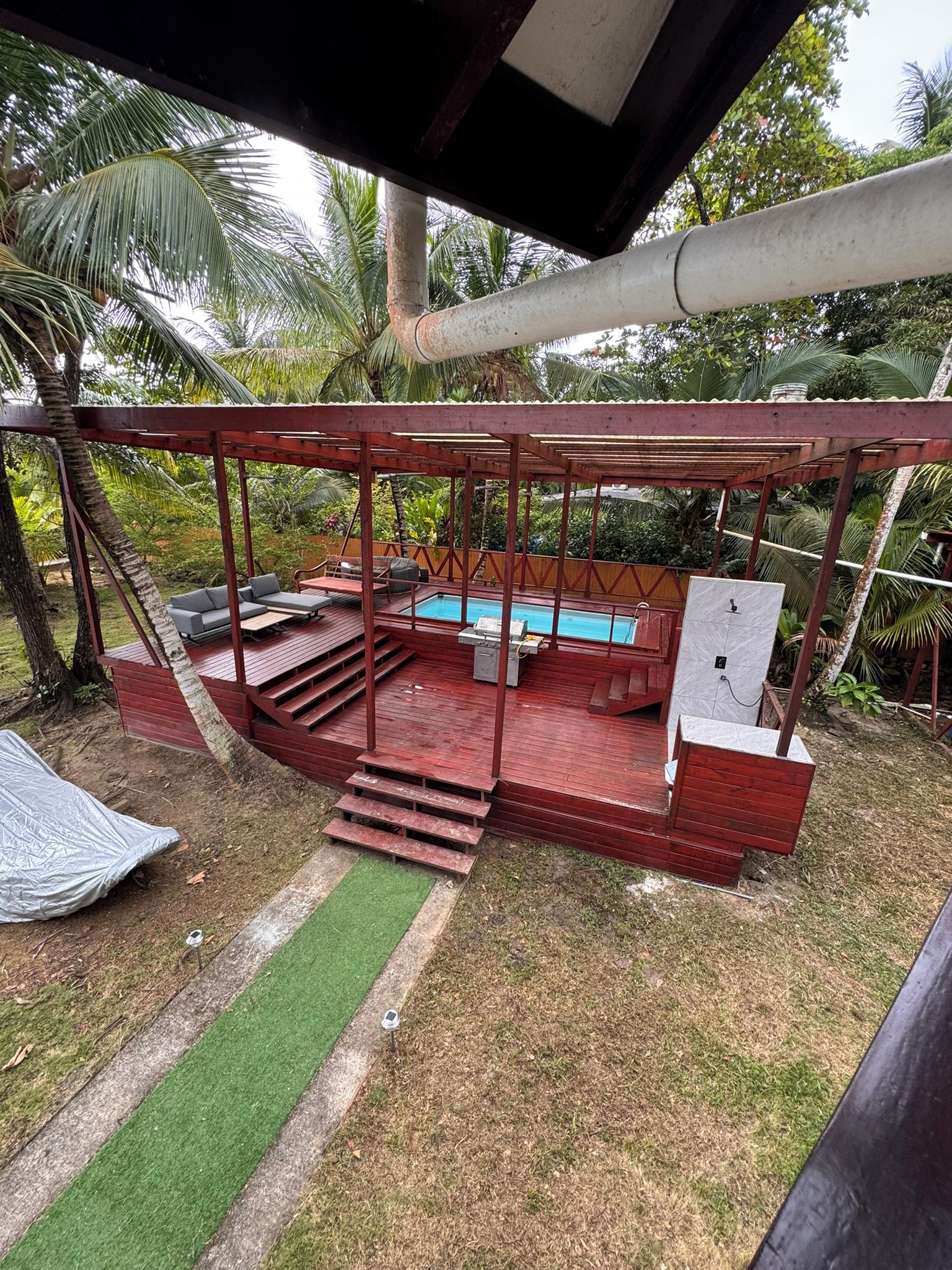 Un espacio exterior techado con piscina, mobiliario y escalones que conducen a una terraza.