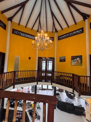 A spacious interior with a high ceiling, a central chandelier, and a balcony overlooking a lower level.