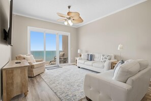 A spacious living area with a large window, a ceiling fan, and a view of the ocean. - Windemere 1407 (Pensacola)