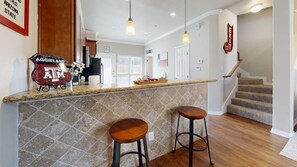 A kitchen with a stone backsplash, two bar stools, a countertop, and a Texas A&M logo.