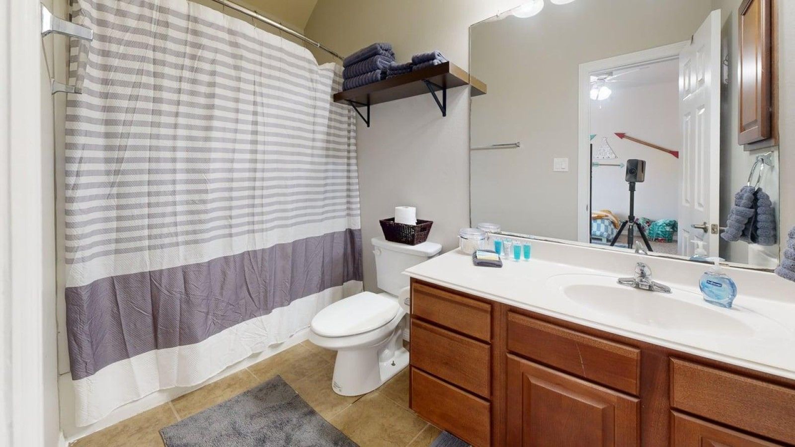 Une salle de bain avec un rideau de douche à rayures, des toilettes, un lavabo avec un miroir et des meubles en bois.