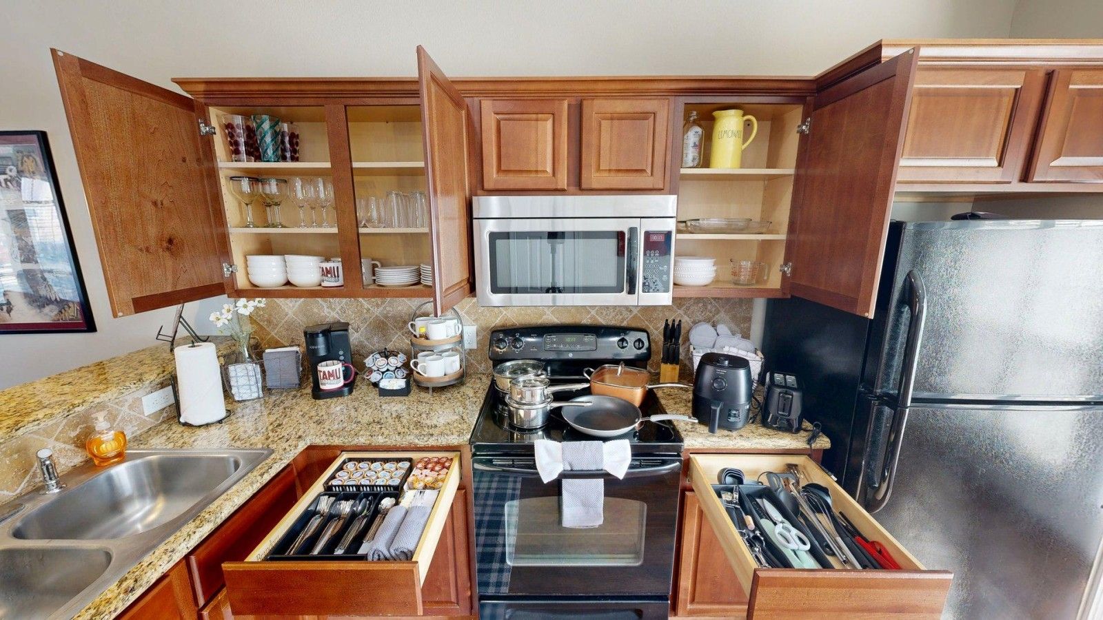 A modern kitchen with wooden cabinets, a stainless steel refrigerator, a microwave, a stove, and a coffee maker.