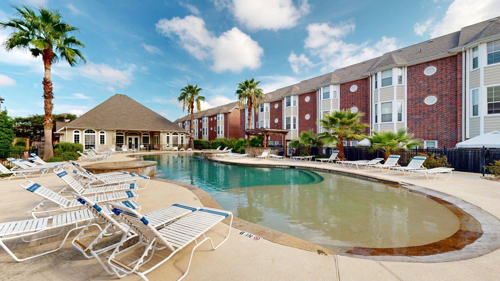 A swimming pool with lounge chairs, a brick building, and palm trees.