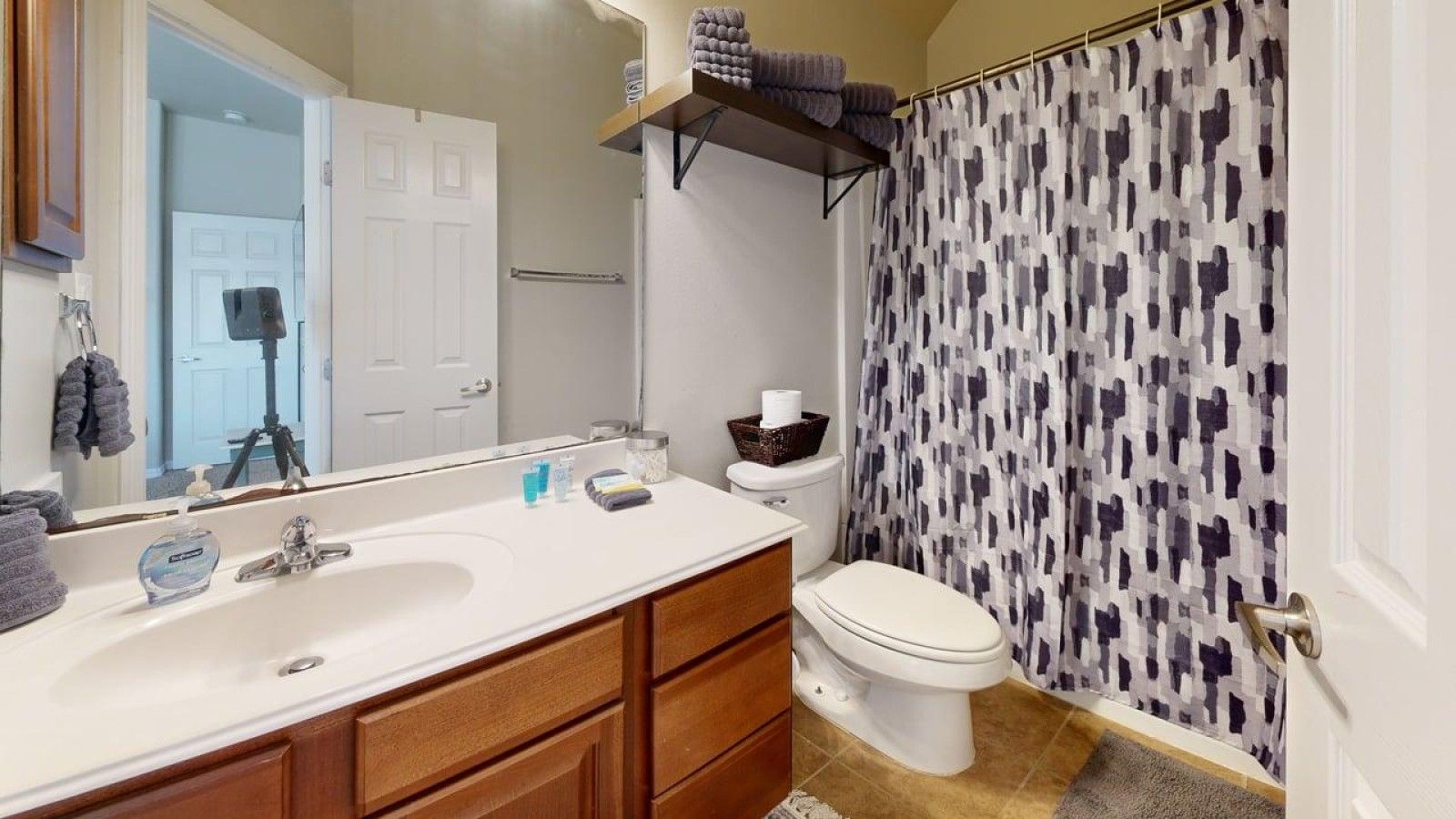 Une salle de bain avec un lavabo blanc, un meuble-lavabo en bois, des toilettes et un rideau de douche à motifs géométriques.