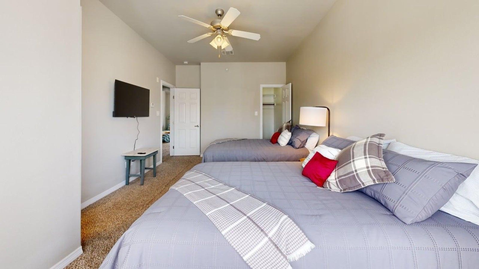 A bedroom with two beds, a ceiling fan, a TV, and a bedside table.