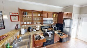 Eine Küche mit Granit Arbeitsplatten, einer Edelstahl-Spüle, Holzschränken, einer Mikrowelle, einem Herd und einem Kühlschrank.
