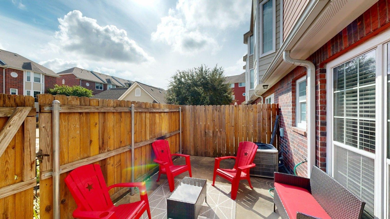 Une terrasse avec une clôture en bois, des chaises rouges et une table.