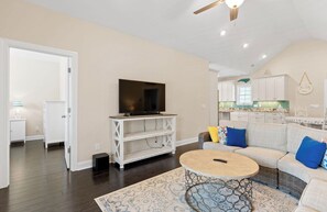 A living room with a television on a white stand, a round coffee table, and a sofa with blue cushions. - Private Saltwater Pool within Walking Distance to the Beach Oak Island NC (Oak Island)