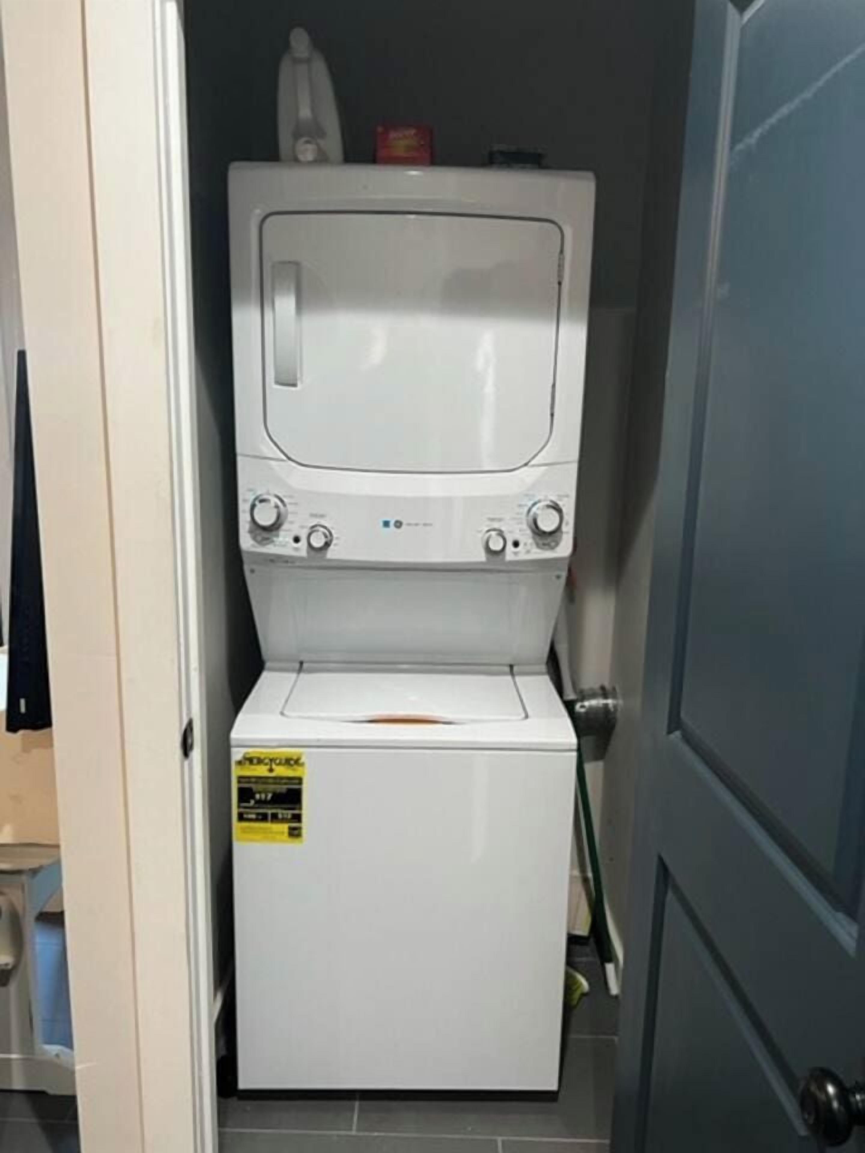A compact washer and dryer unit with a control panel, a yellow sticker, and a small storage compartment.