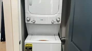A compact washer and dryer unit with a control panel, a yellow sticker, and a small storage compartment.