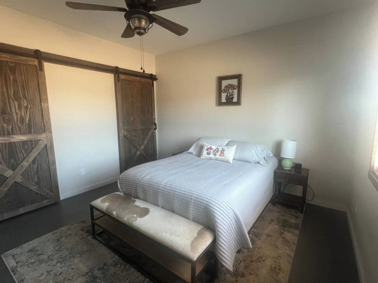 Une chambre à coucher comprenant un lit, un banc, une table de chevet, une lampe et un ventilateur de plafond.