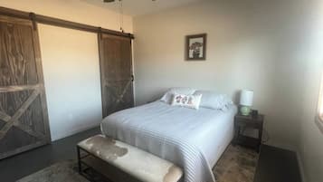 Une chambre à coucher comprenant un lit, un banc, une table de chevet, une lampe et un ventilateur de plafond.