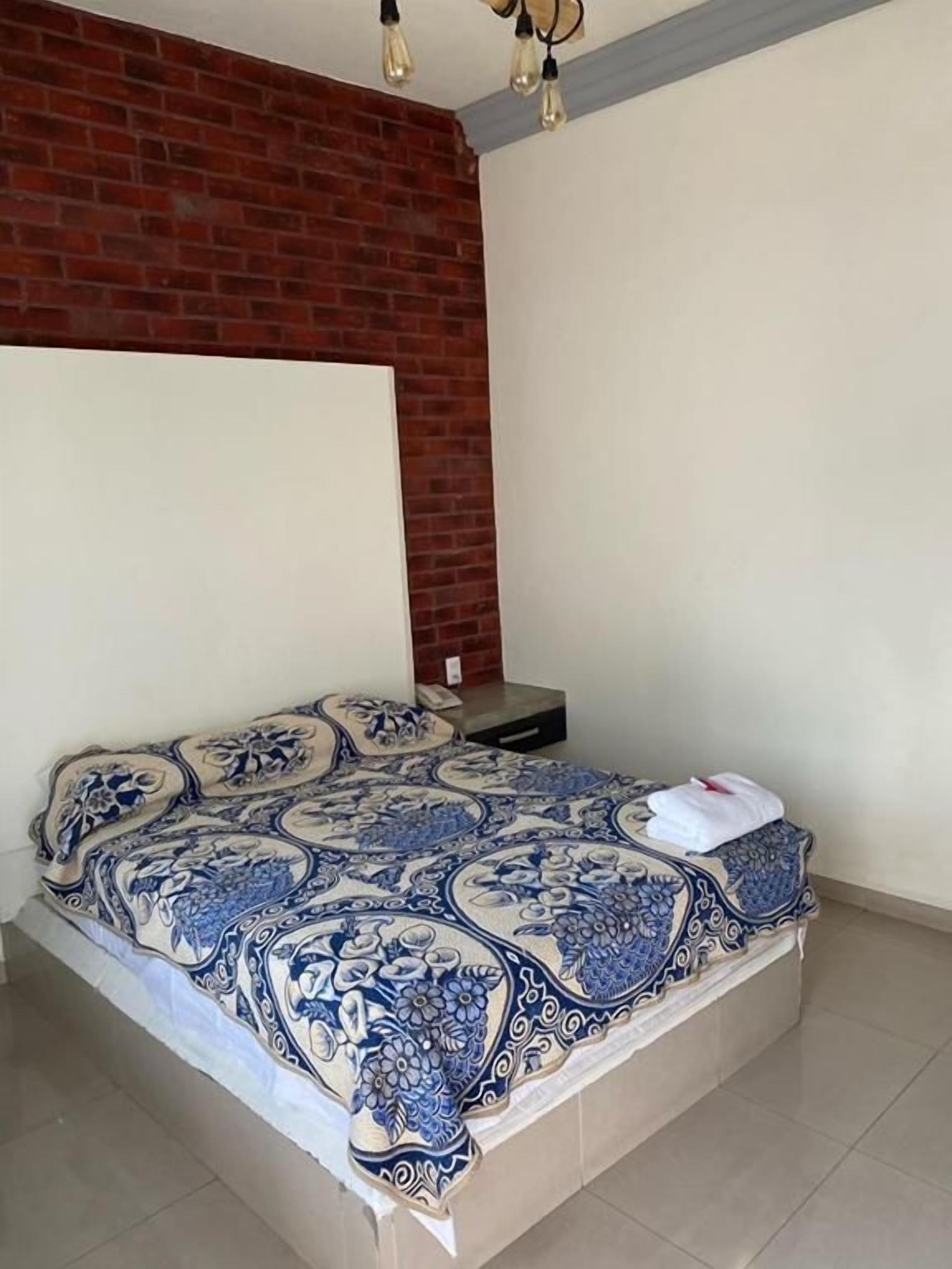 Un dormitorio con una cama, una pared de ladrillo y una lámpara.