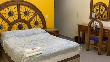 A bedroom with a bed, a wooden headboard, a bedside table, a chair, and a mirror.