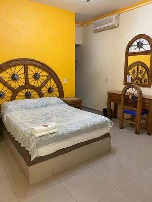 Un dormitorio con cama, cabecera de madera, mesita de noche, silla y espejo.