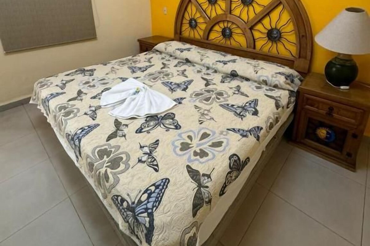 A bedroom with a bed, a nightstand, a lamp, and a window with a blind.