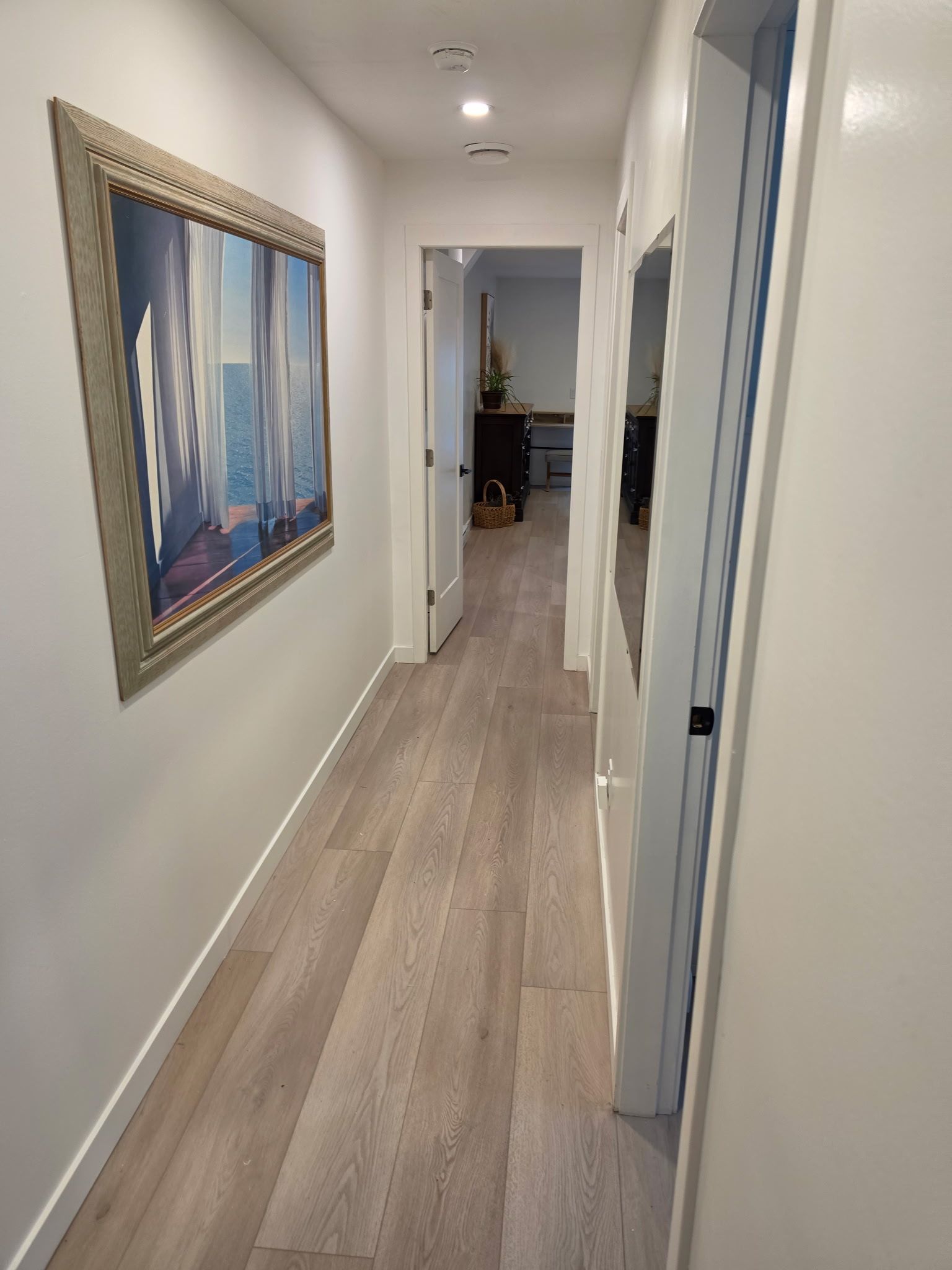 Ein Flur mit Holzboden, einem gerahmten Gemälde an der Wand und einer Tür zu einem Zimmer.