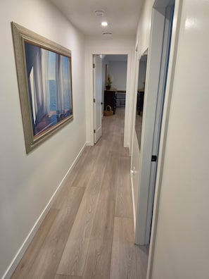 Un passadís amb terra de fusta, un quadre amb marc a la paret i una porta que dona a una habitació.