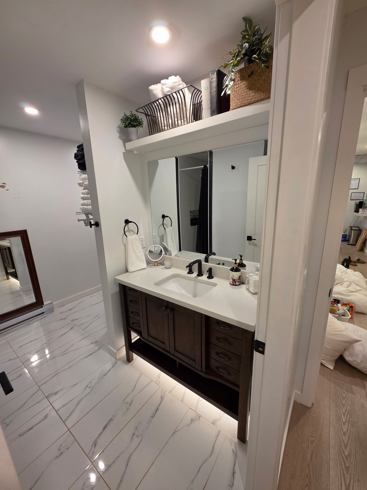 Une salle de bain moderne avec un sol en marbre blanc, un grand miroir, un meuble-lavabo en bois foncé et un luminaire au plafond.