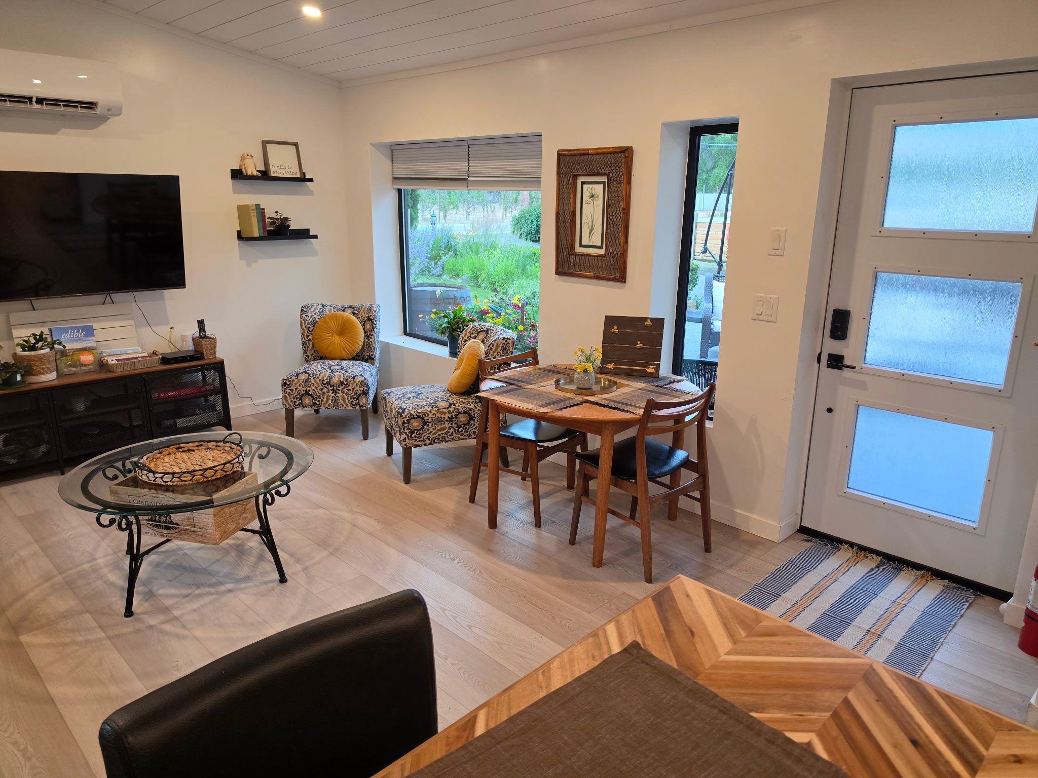 Een woonkamer met een televisie, een eettafel, stoelen, een open haard en uitzicht op de omgeving.