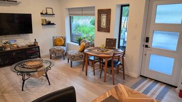 Een woonkamer met een televisie, een eettafel, stoelen, een open haard en uitzicht op de omgeving.