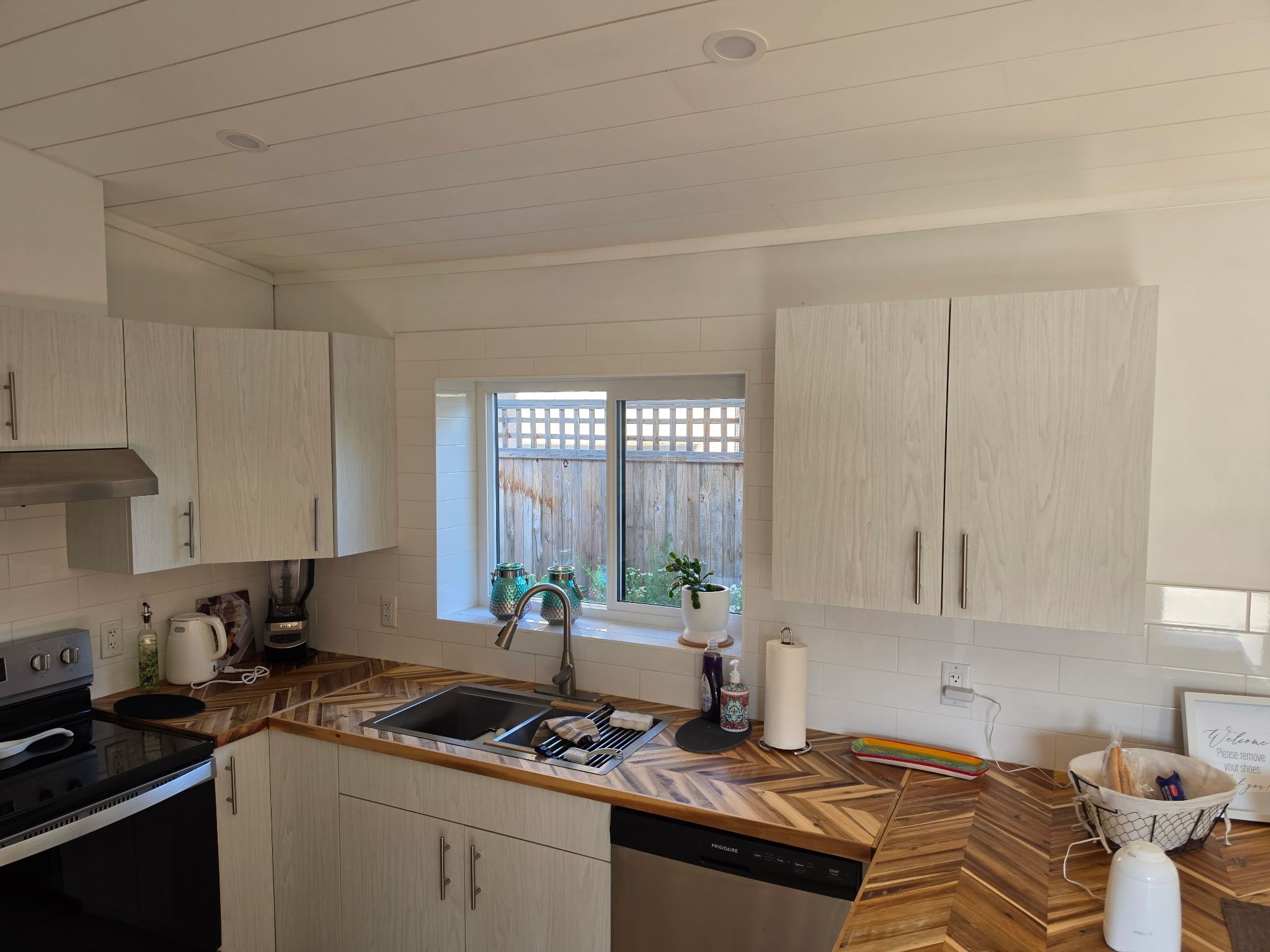 Ett modernt kök med träskåp, en inbyggd diskmaskin och ett fönster med utsikt över grönområden.