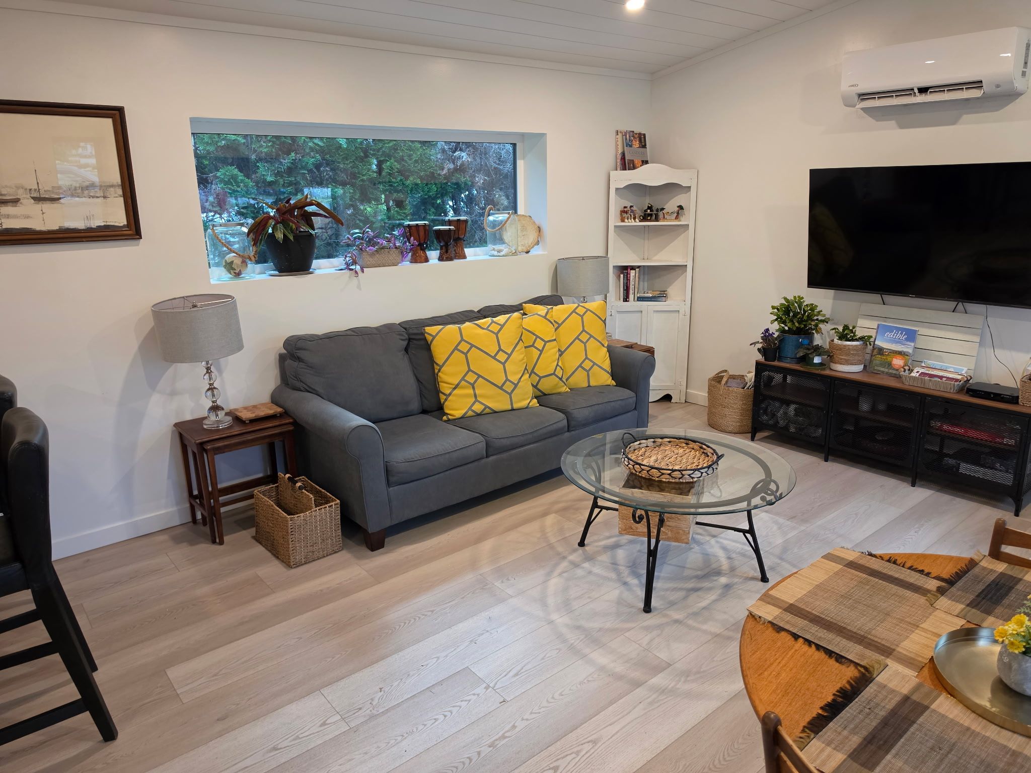 A living room with a grey sofa, a glass coffee table, a TV, and a bookshelf.