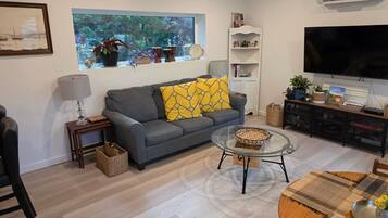 A living room with a grey sofa, a glass coffee table, a TV, and a bookshelf.