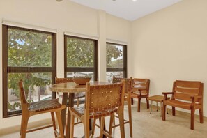 Ein Zimmer mit einem runden Tisch, Holzstühlen und großen Fenstern mit Jalousien.