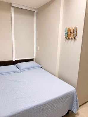 A bedroom with a bed, a window with blinds, and a wall-mounted shelf with decorative items.