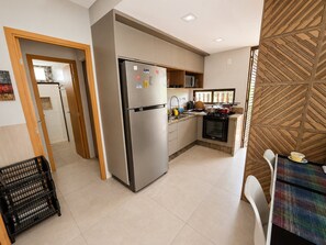 A compact kitchen with a stainless steel refrigerator, a built-in oven, and a small dining area with a colorful table.