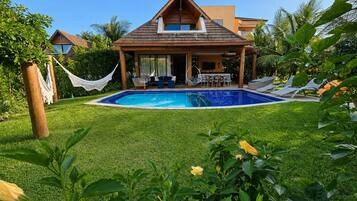 Uma casa com piscina, varanda coberta e vegetação exuberante.