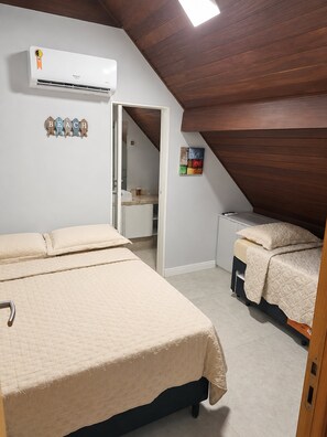 A bedroom with a sloped ceiling, a bed, a bedside table, a small desk, and an air conditioning unit.
