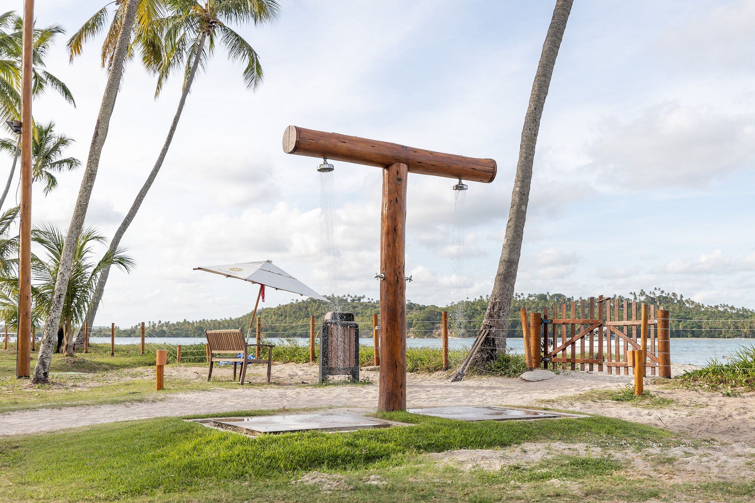 Une structure en bois agrémentée d’un élément aquatique, entourée de palmiers et offrant une vue sur une étendue d’eau.