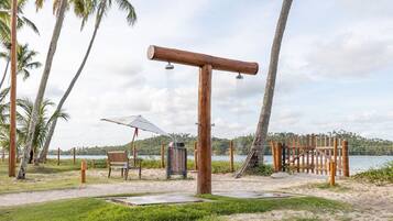 Une structure en bois agrémentée d’un élément aquatique, entourée de palmiers et offrant une vue sur une étendue d’eau.