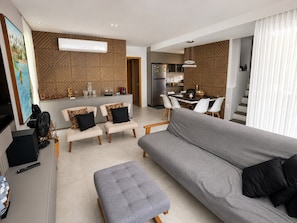 A modern living room with a grey sofa, two armchairs, a coffee table, and a dining area with a table and chairs.