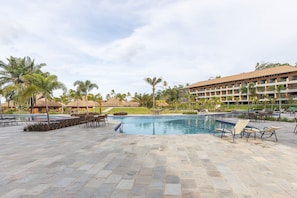A resort pool area with lounge chairs, a swimming pool, and a building with multiple balconies.