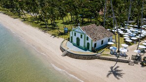 A beachside building with a white facade and green trim, adjacent to a sandy beach and palm trees.