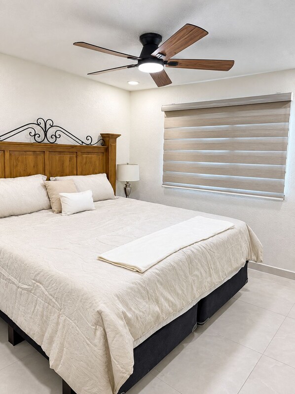 A bedroom with a bed, a ceiling fan, a bedside lamp, and a window with blinds.