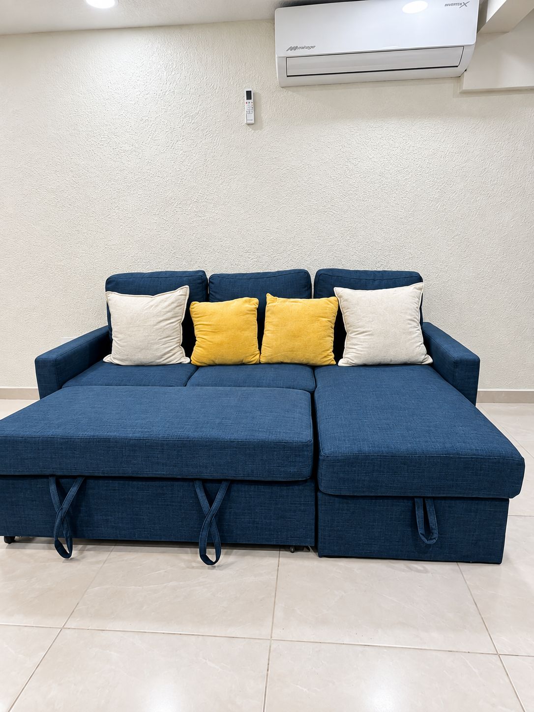 Um sofá modular com unidade de armazenamento embutida, um ar condicionado fixado na parede e uma parede texturizada.