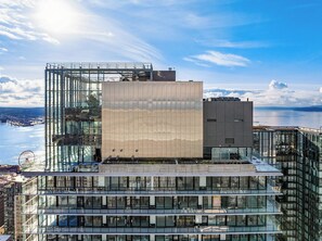 A modern building with a glass facade, a central courtyard, and a view of the water. - Executive Living with Resort Amenities (Seattle)