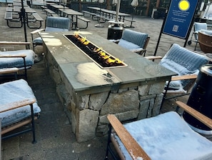 Een terras met stenen tafels en stoelen, een vuurplaats en een bord met een QR-code.