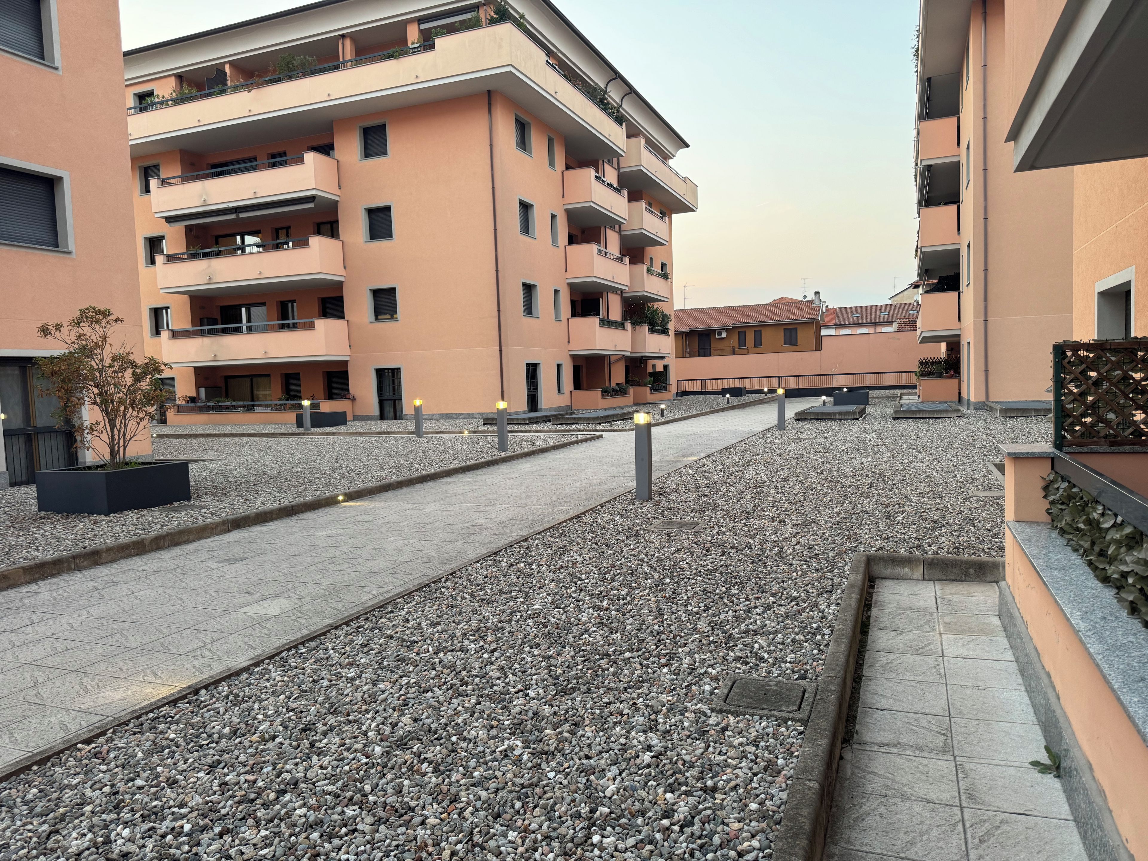 En bostadsbyggnad med flera balkonger, en stenlagd innergård och en liten trädgårdsyta.
