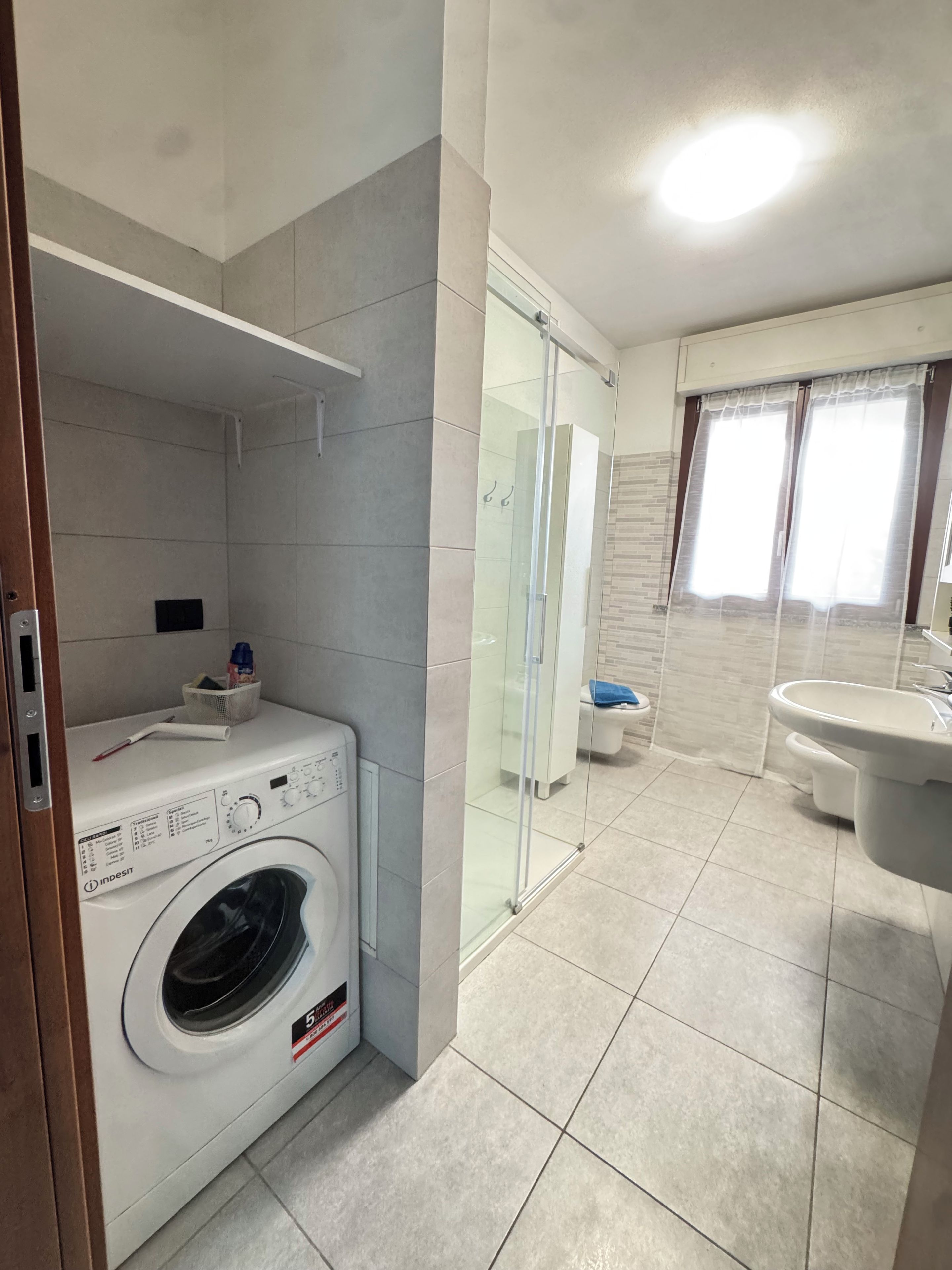 A modern bathroom with a washing machine, glass shower enclosure, and a sink.