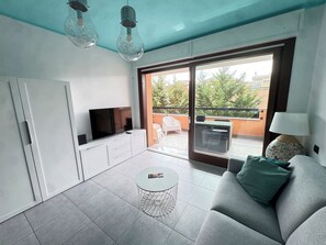 A modern living room with a flat-screen TV, a sofa, a round coffee table, and a balcony with outdoor furniture.
