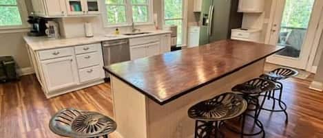 A kitchen with a large island, bar stools, and white cabinetry.