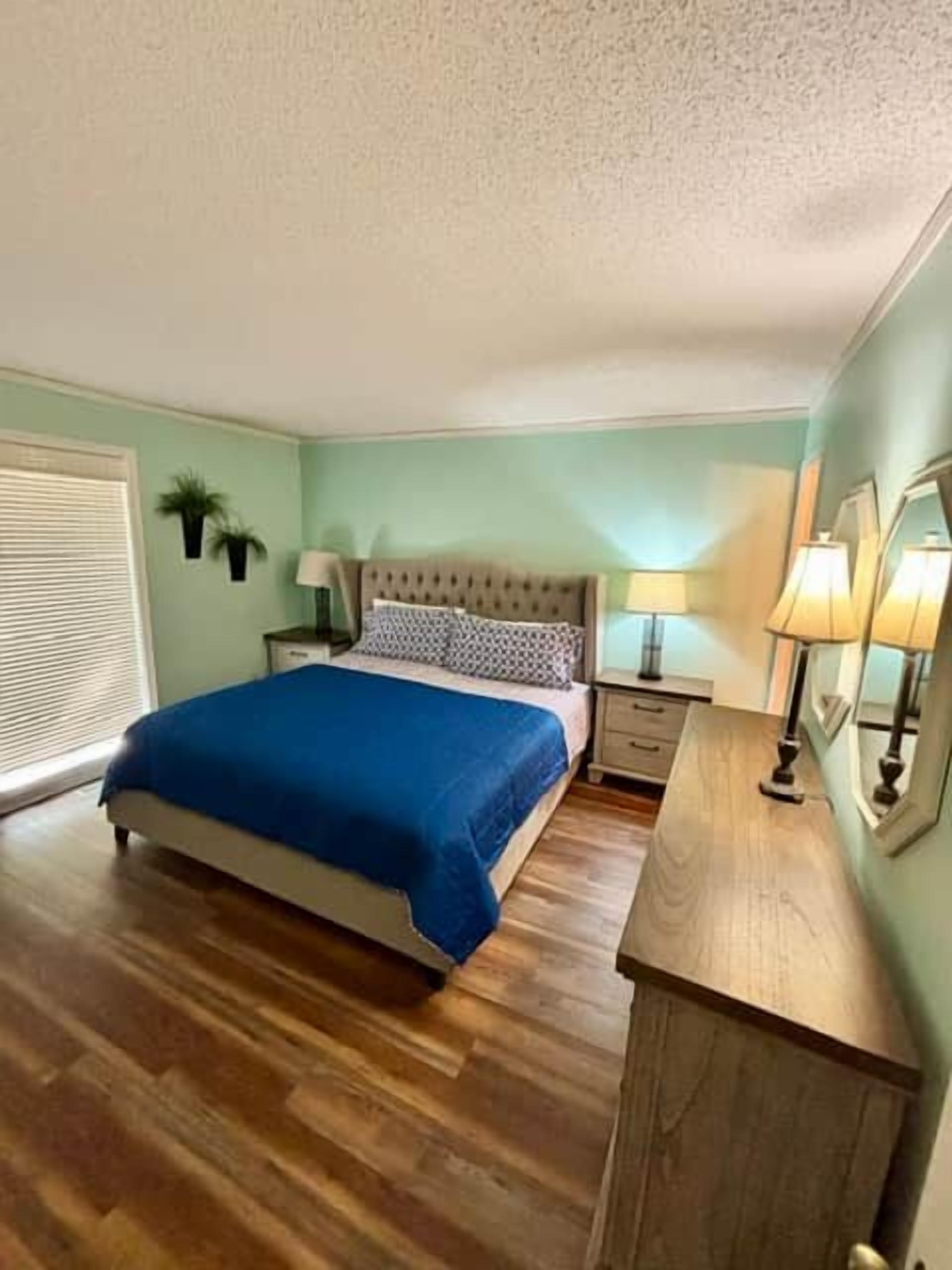 Een slaapkamer met een bed, nachtkastjes, een lamp en een spiegel.